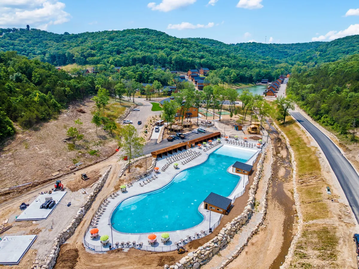 An inviting exterior view of a large swimming pool surrounded by poolside lounge chairs, lush greenery, and nearby buildings. The scene is lively yet relaxed, suggesting opportunities for swimming, sunbathing, and social gatherings.