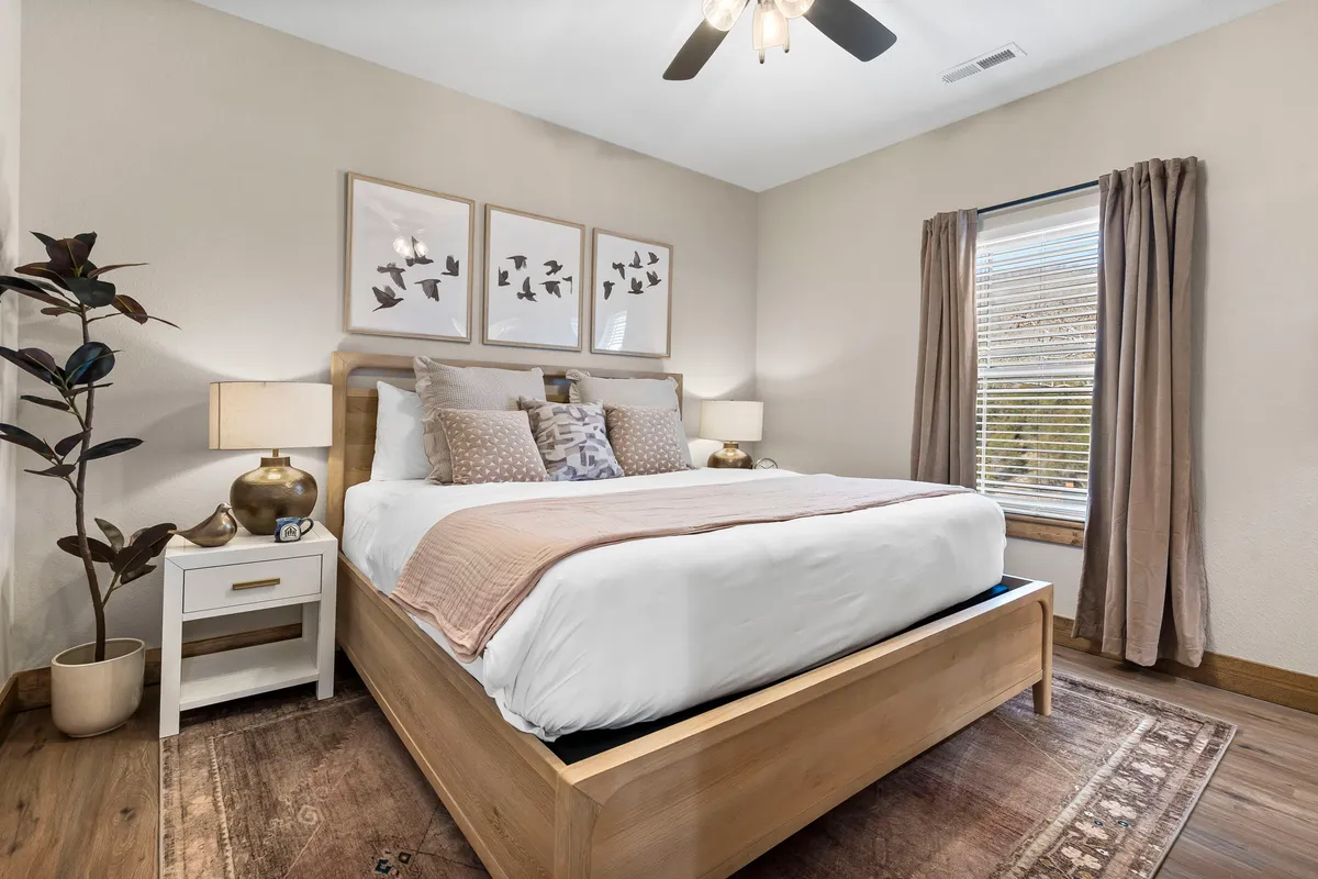 A bedroom featuring a cozy bed, calming artwork on the wall, a window with curtains letting in soft natural light, and side tables with lamps. The atmosphere is restful and welcoming, perfect for unwinding after a long day.
