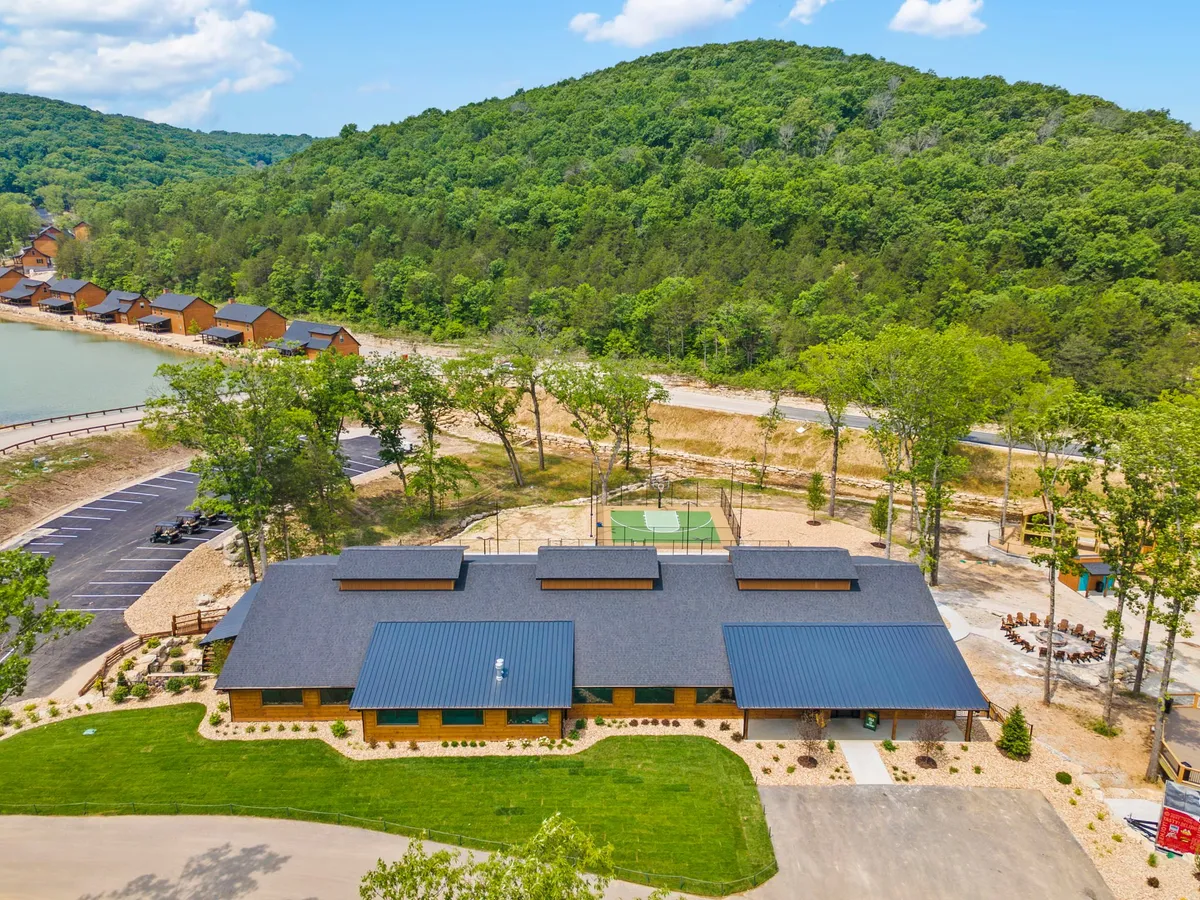 An exterior view showing the resort’s main building, nearby cabins, a basketball court, wooded walking paths, and abundant greenery. The scene is lively and communal, suggesting a range of accessible activities from sports to nature walks.
