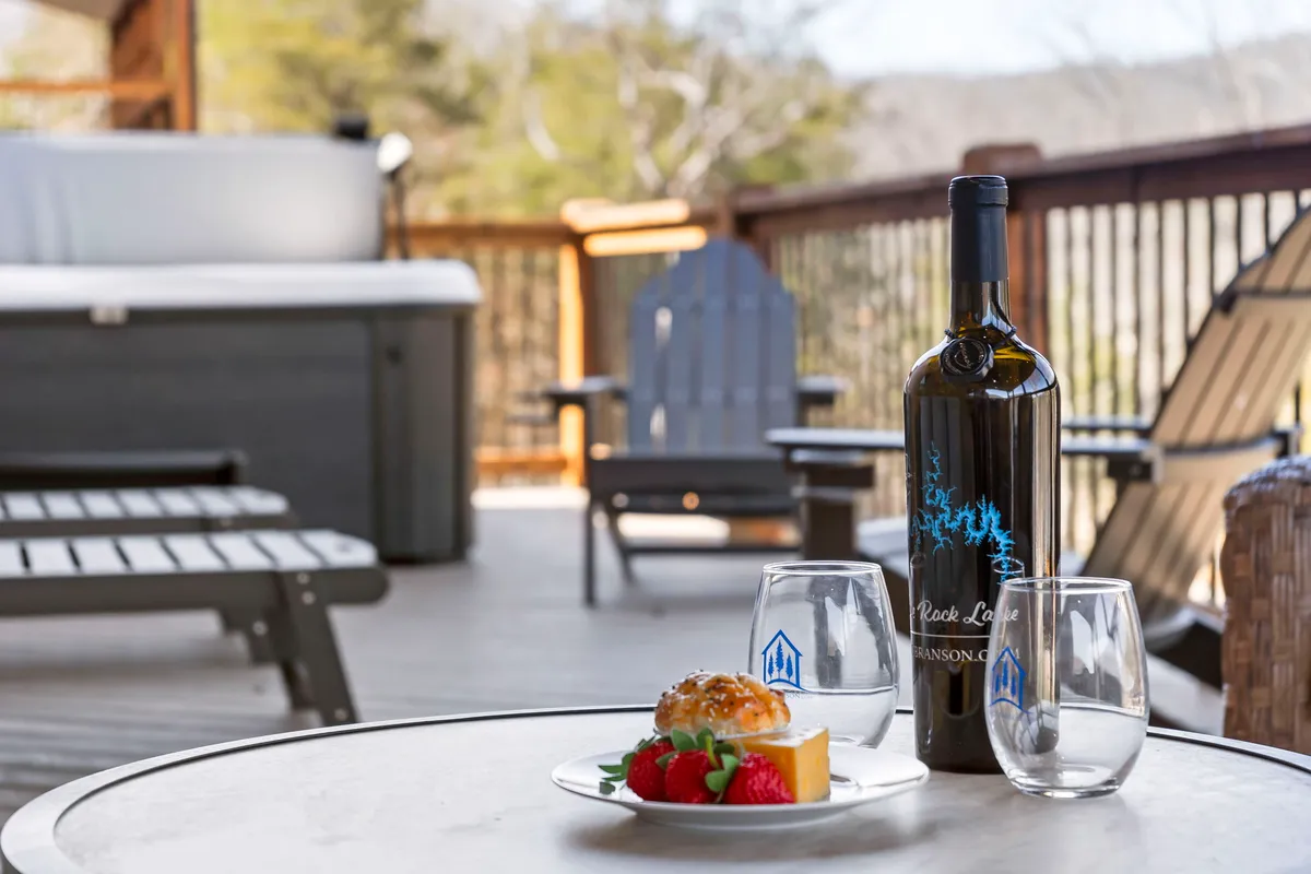 A relaxing outdoor hot tub setup on a deck, complemented by wine, dessert, and deck chairs, with serene natural surroundings. The mood is tranquil and perfect for unwinding after activity-filled days.