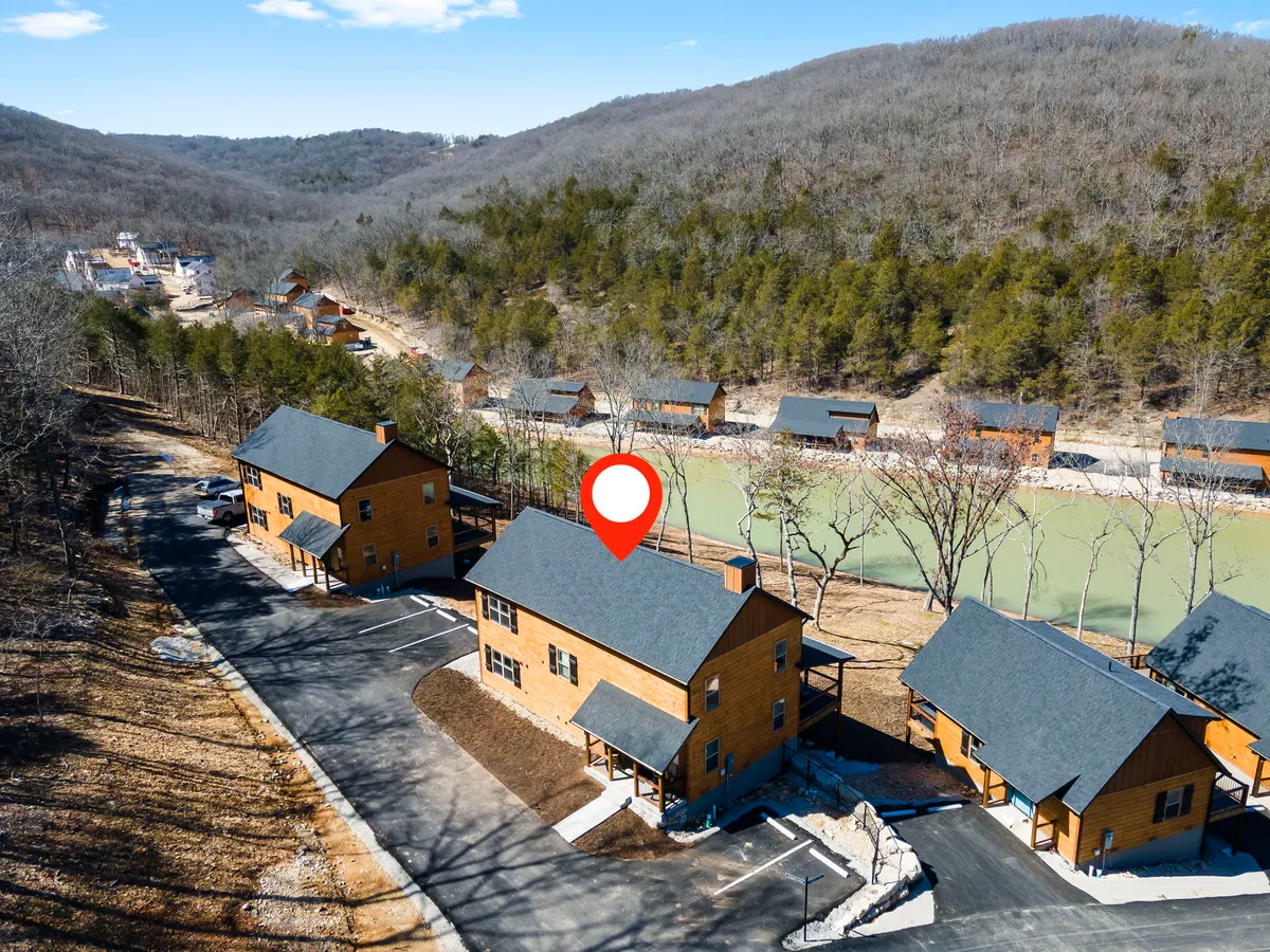 A broad exterior view featuring several wooden cabins nestled among lush greenery, with a calm pond and mountain backdrop. The scene exudes tranquility and invites thoughts of nature walks, wildlife sightings, and peaceful outdoor moments suitable for both pets and owners.