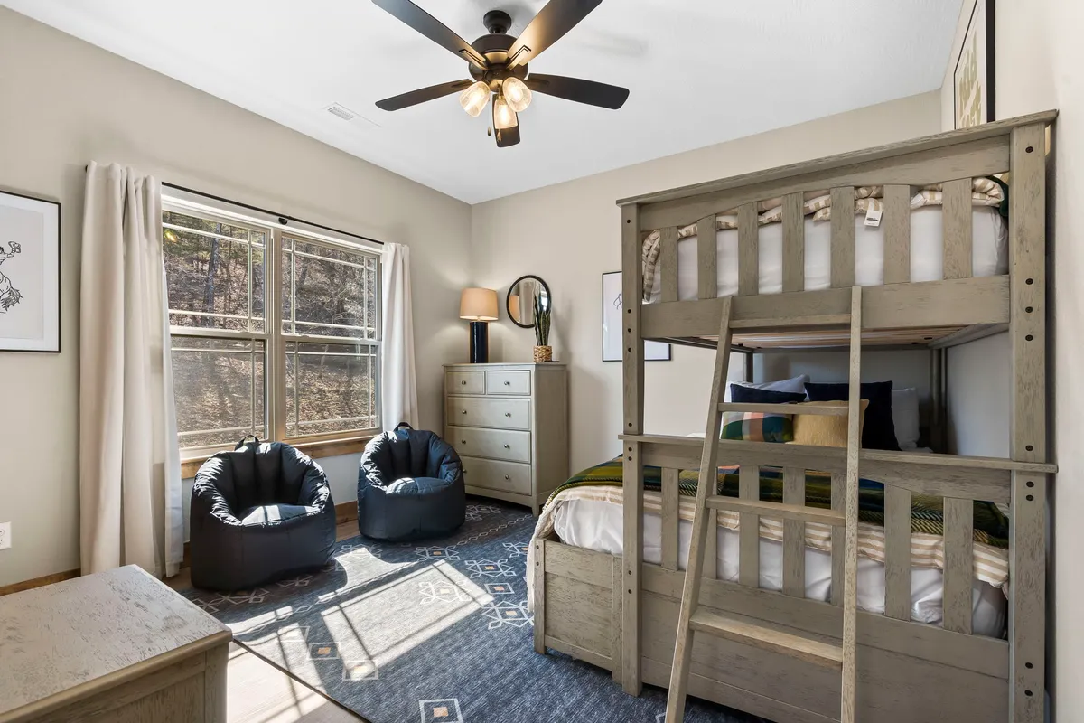 A playful bunk bedroom with a twin-over-full bunk bed, colorful bean bag chairs, a dresser, lamp, and a window. The space feels inviting and specifically designed for younger guests, encouraging relaxation and imaginative play.