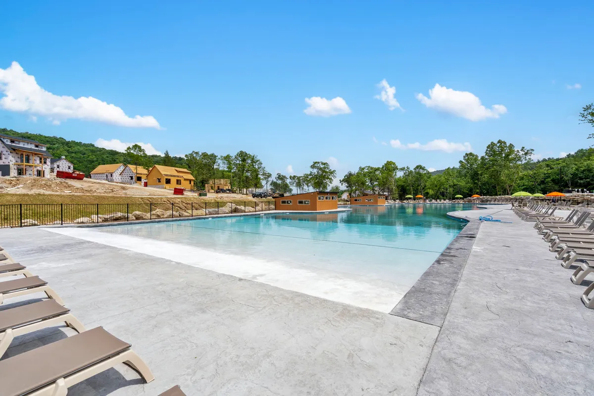 An inviting outdoor swimming pool surrounded by lounge chairs and cabana-style buildings, all set amidst lush trees. The scene exudes a leisurely and serene vibe, ideal for sunbathing or enjoying a quiet swim under the open sky.